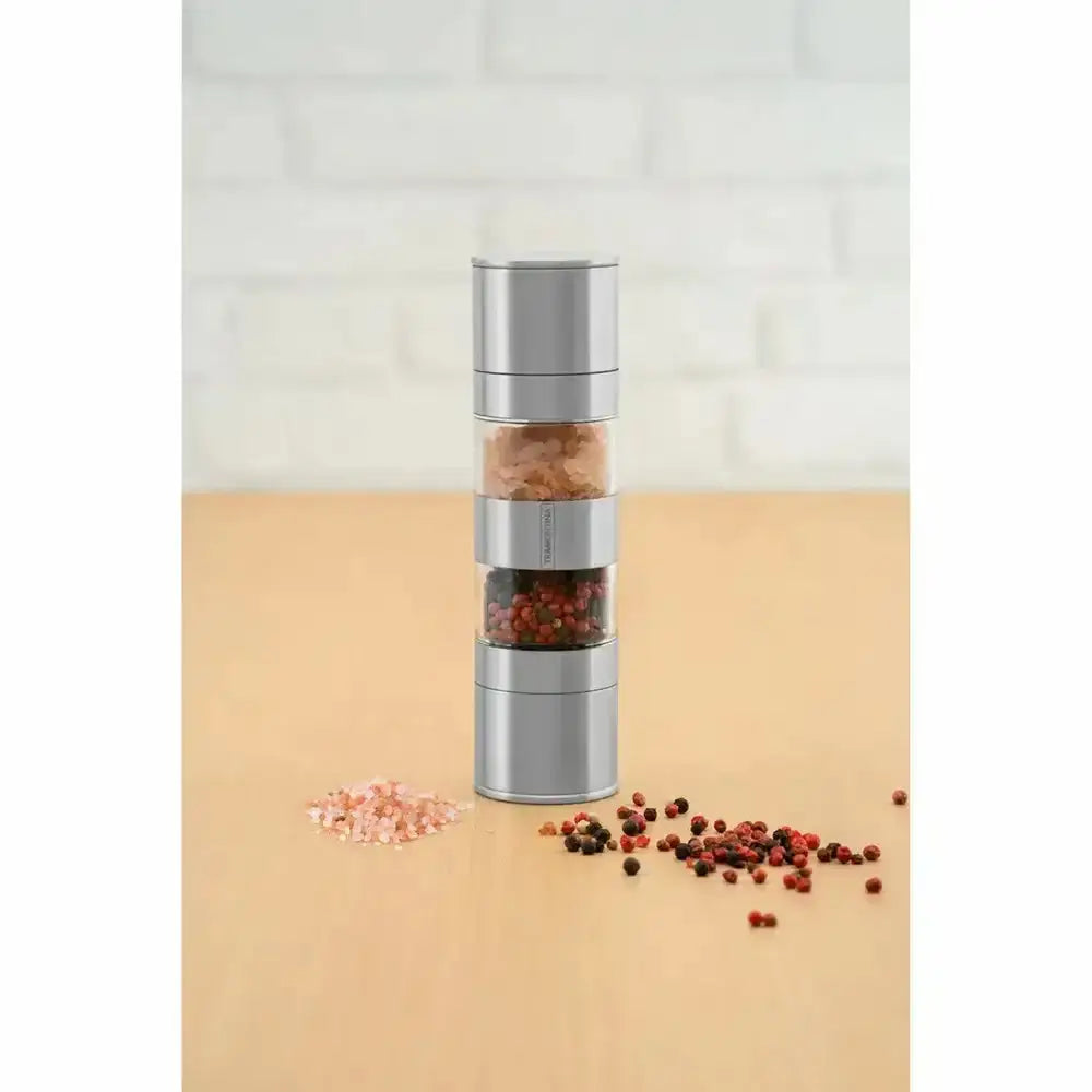 Silver pepper grinder with peppercorns on a beige surface
