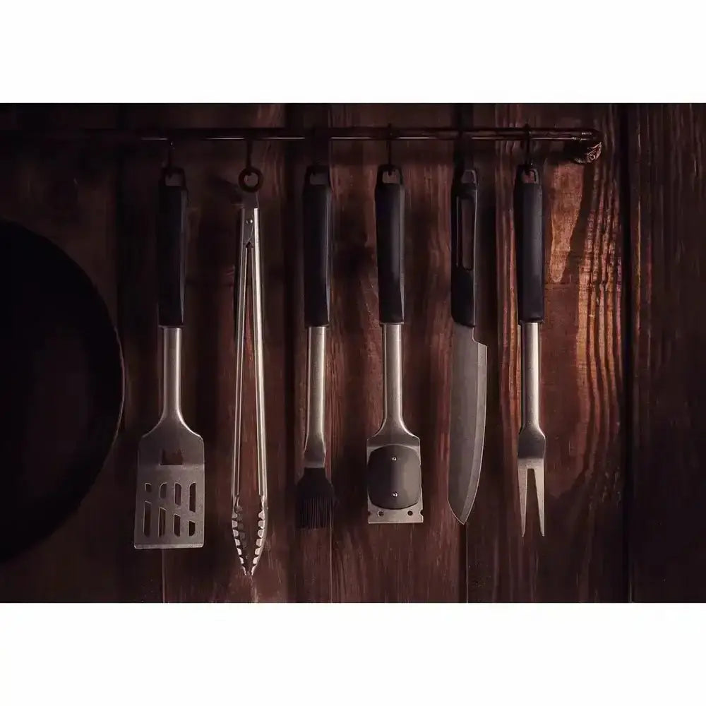 Set of barbecue tools including tongs, spatulas, and skewers on a wooden surface.