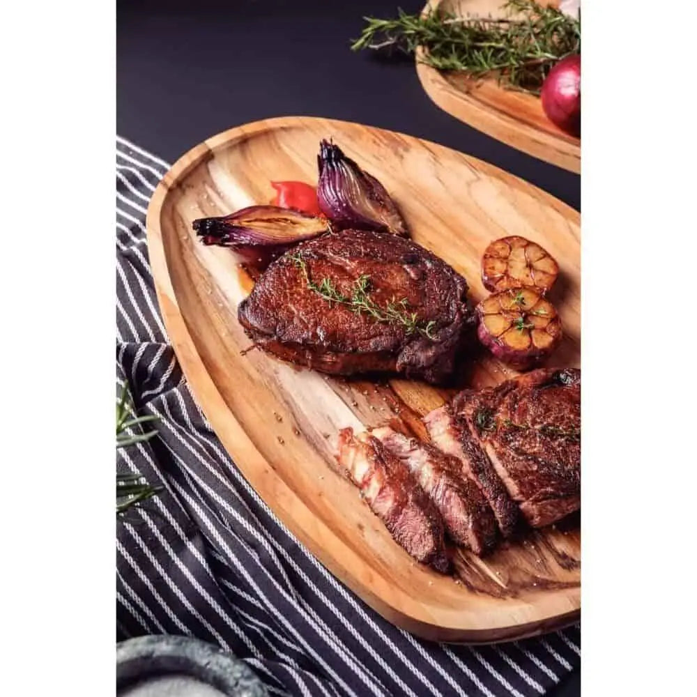 Grilled steak, roasted garlic, and onions served on a wooden serving board