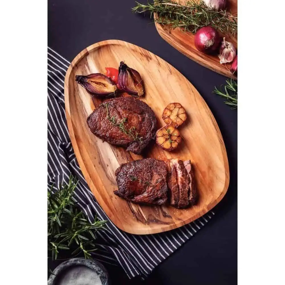 Teakwood serving board with grilled steaks, roasted garlic, and vegetables