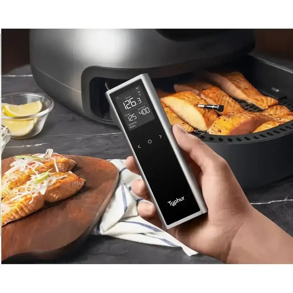 Hand holding a digital thermometer in front of air-fried salmon in an air fryer.