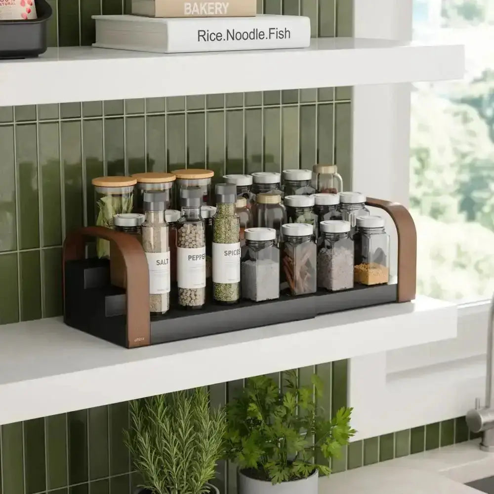 Spice rack with labeled jars on a kitchen shelf with green tiles and plants.