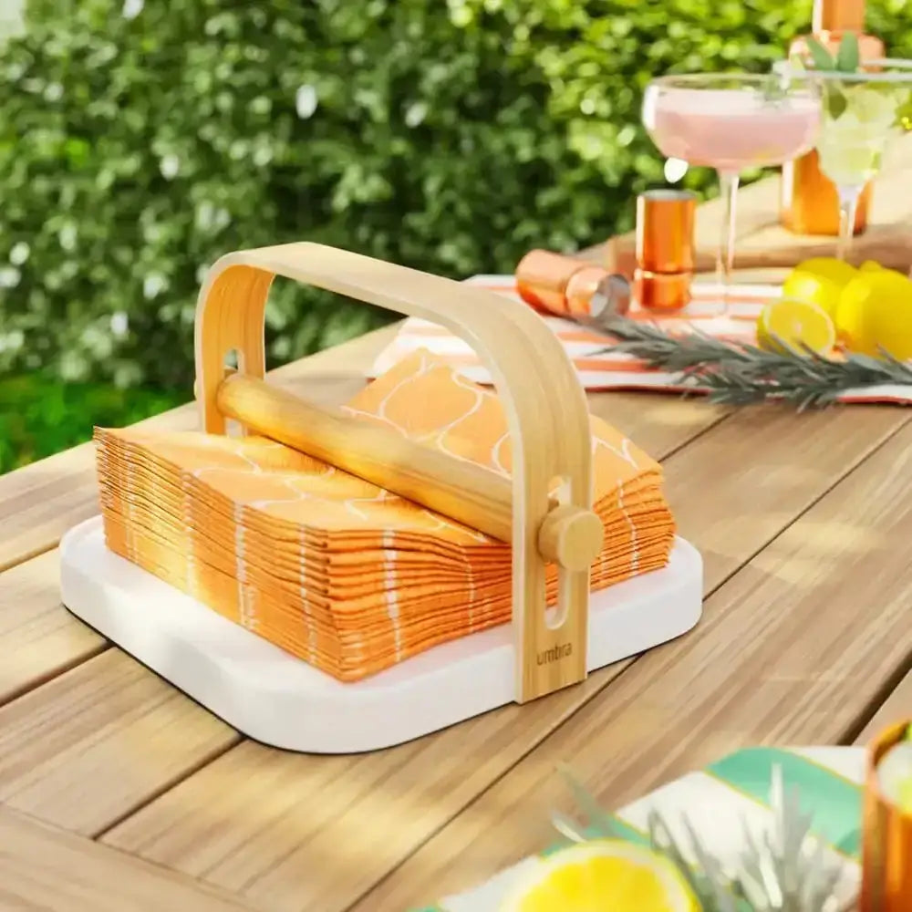 Stack of orange napkins in a wooden holder on a wooden table outdoors.