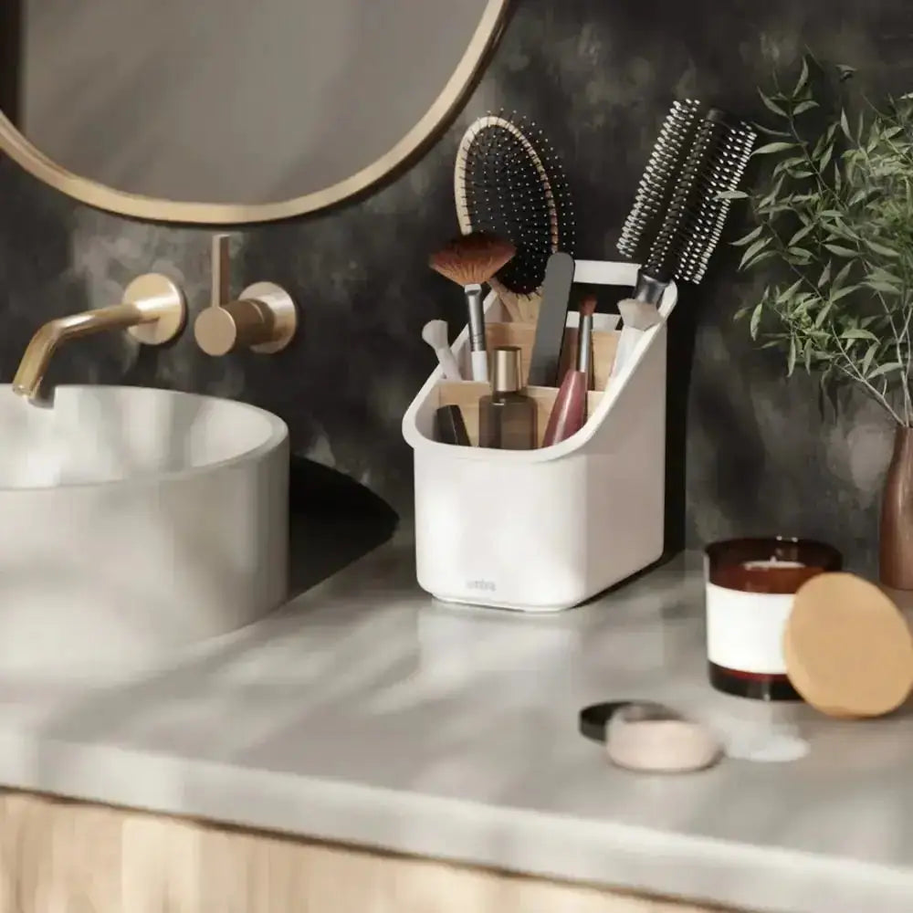 Bathroom counter with makeup brushes in a holder, candle, and plant.