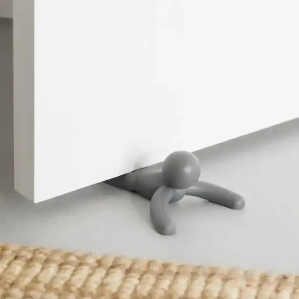Gray door stopper on a white surface with a woven mat at the bottom.