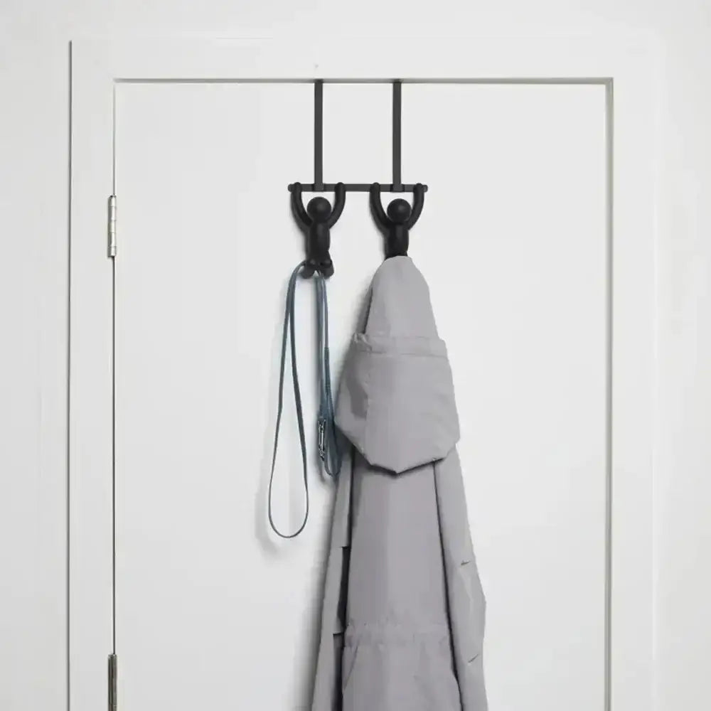 Black metal hook rack with two hooks on a white door, holding a gray coat and a dog leash.