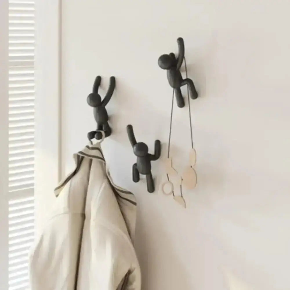 Black wall hooks shaped like people on a white wall with a coat hanging from one of them.