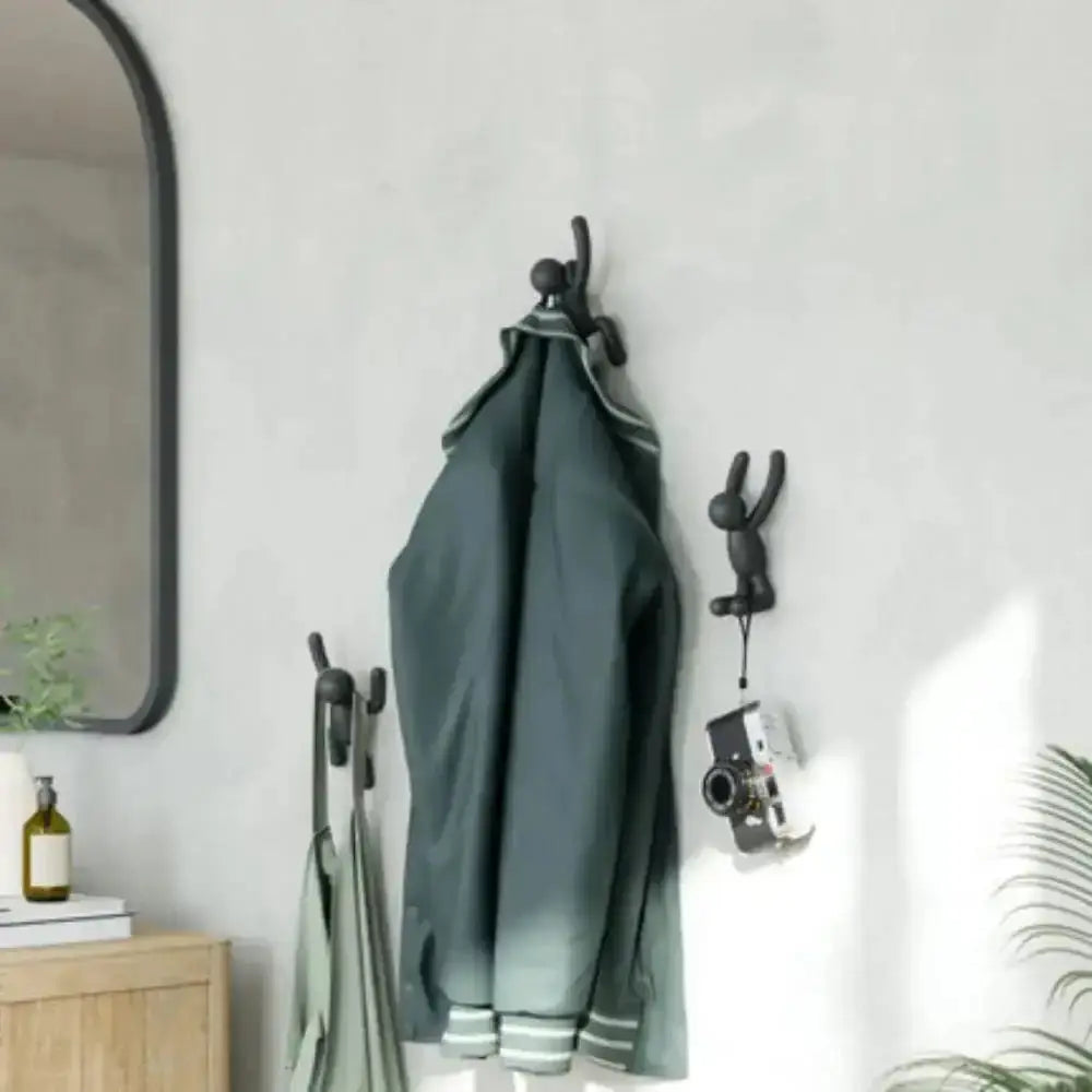 Green coat hanging on a wall-mounted hook with a mirror and plant in the background