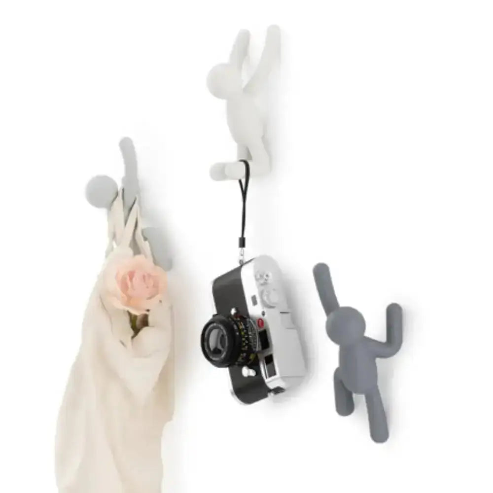 White and gray wall hooks with a camera, scarf, and small figure on a white background