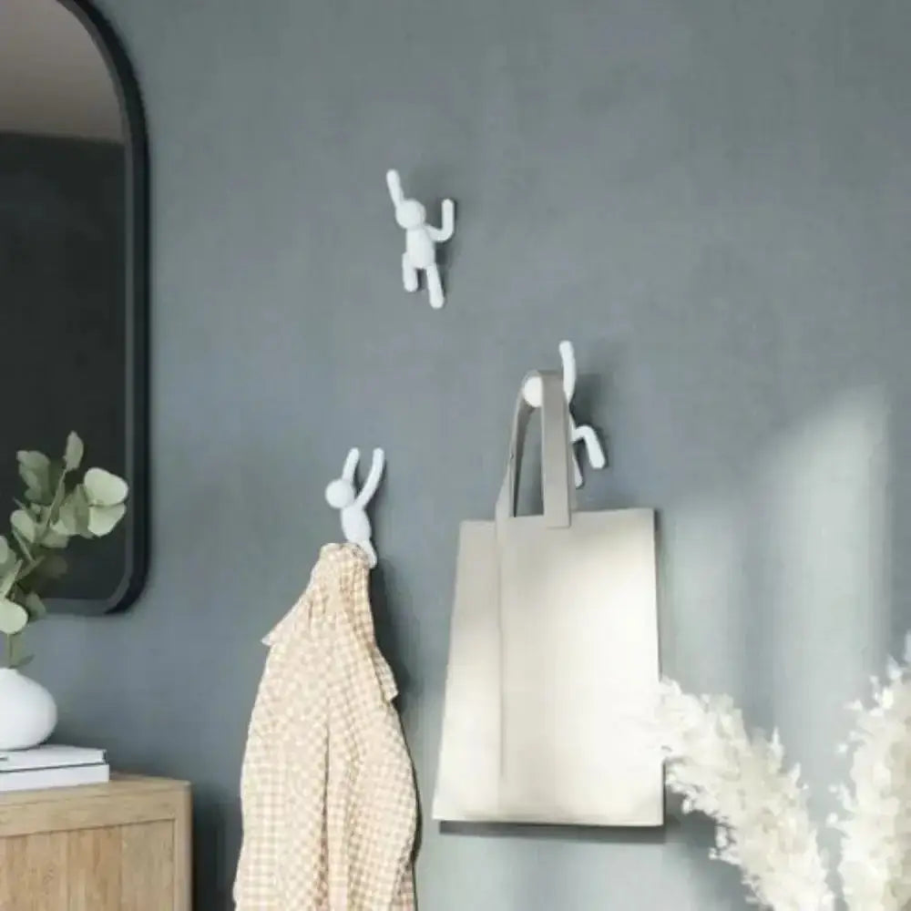 White wall hooks on a gray wall with a tote bag and plant decorations.