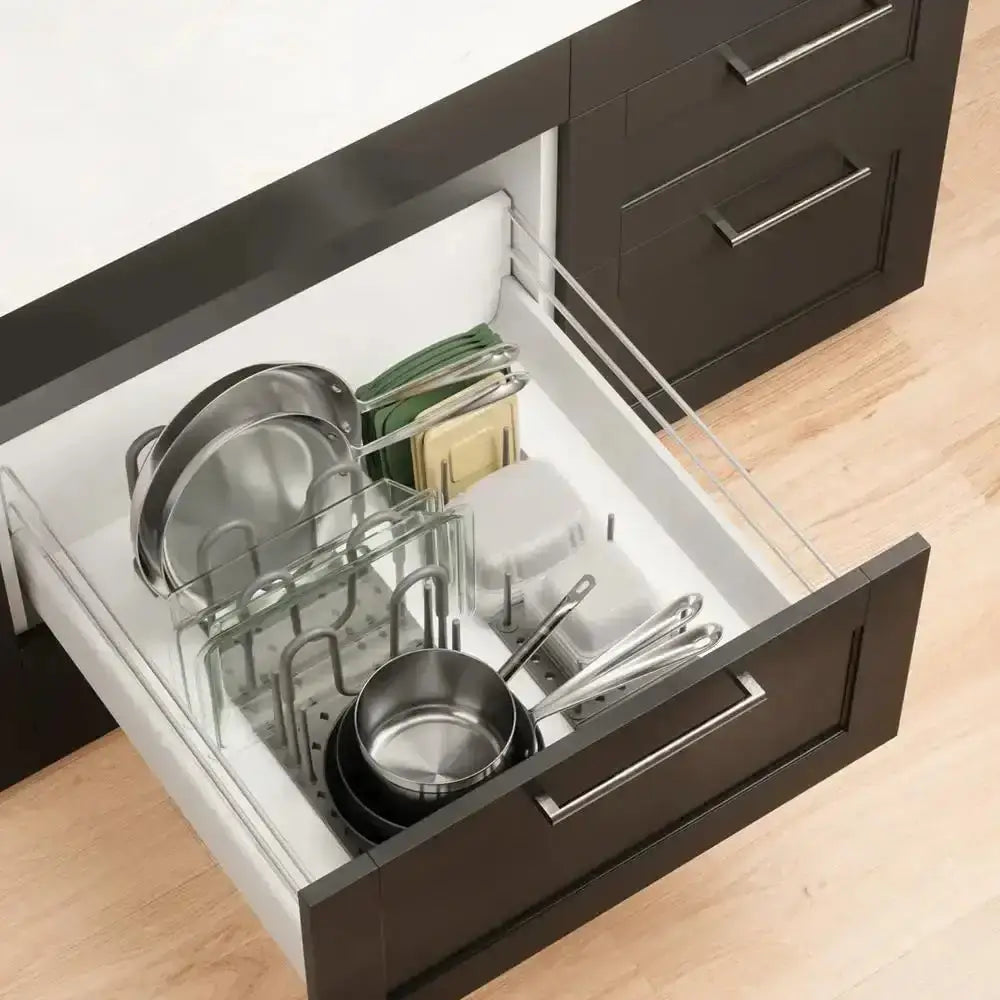 Open kitchen drawer with utensils and cookware on a wooden floor.