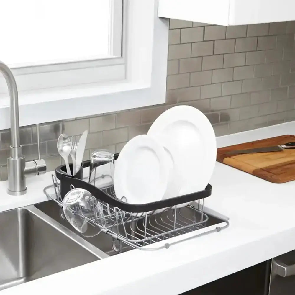 Dish rack with plates, glasses, and cutlery on a kitchen counter next to a sink.