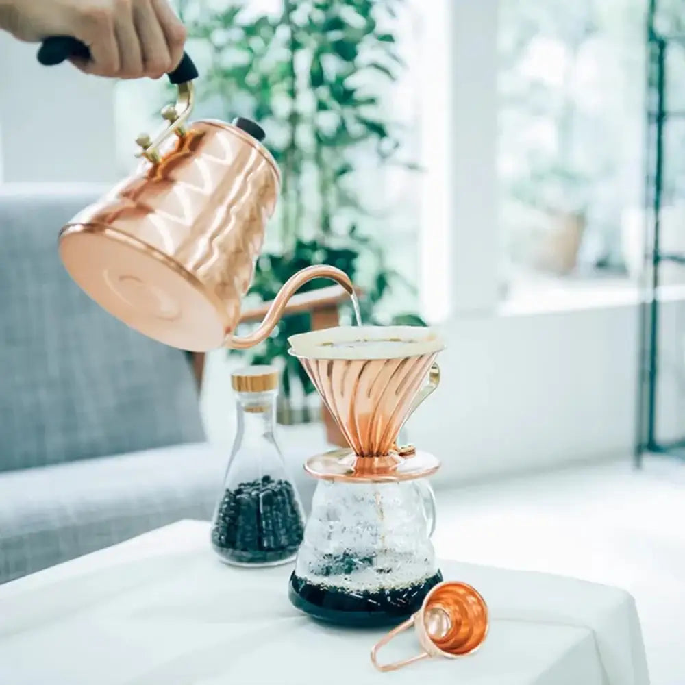 Person pouring coffee into a copper dripper on a table with a blurred background