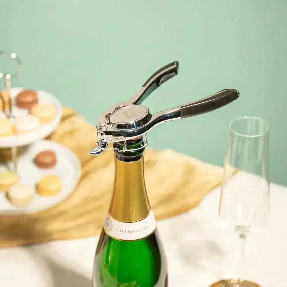 Bottle of champagne with a bottle opener on a table with pastries and a glass.
