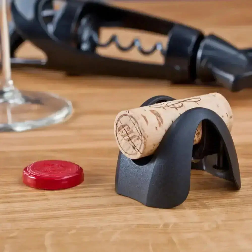 Wine cork and corkscrew on a wooden surface with a glass of wine in the background.