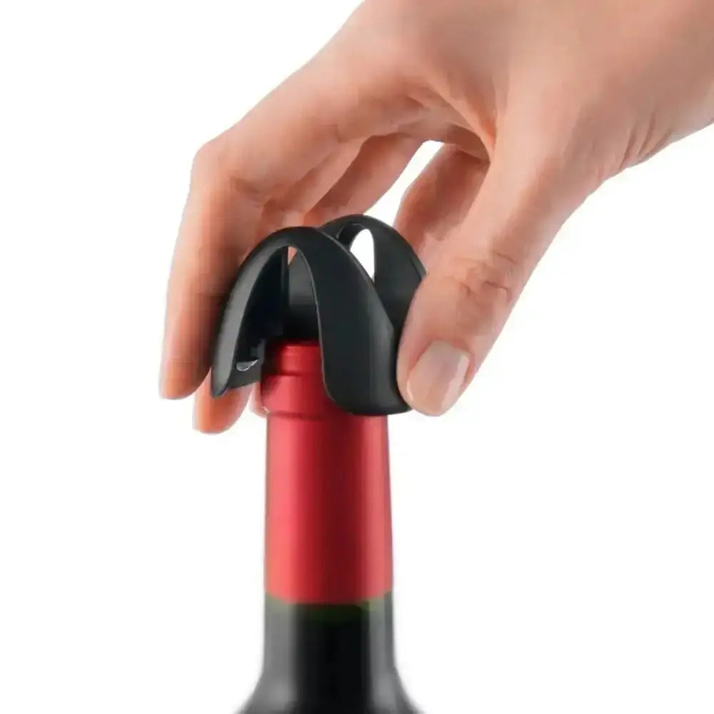 Hand using a black wine foil cutter on a red wine bottle against a white background