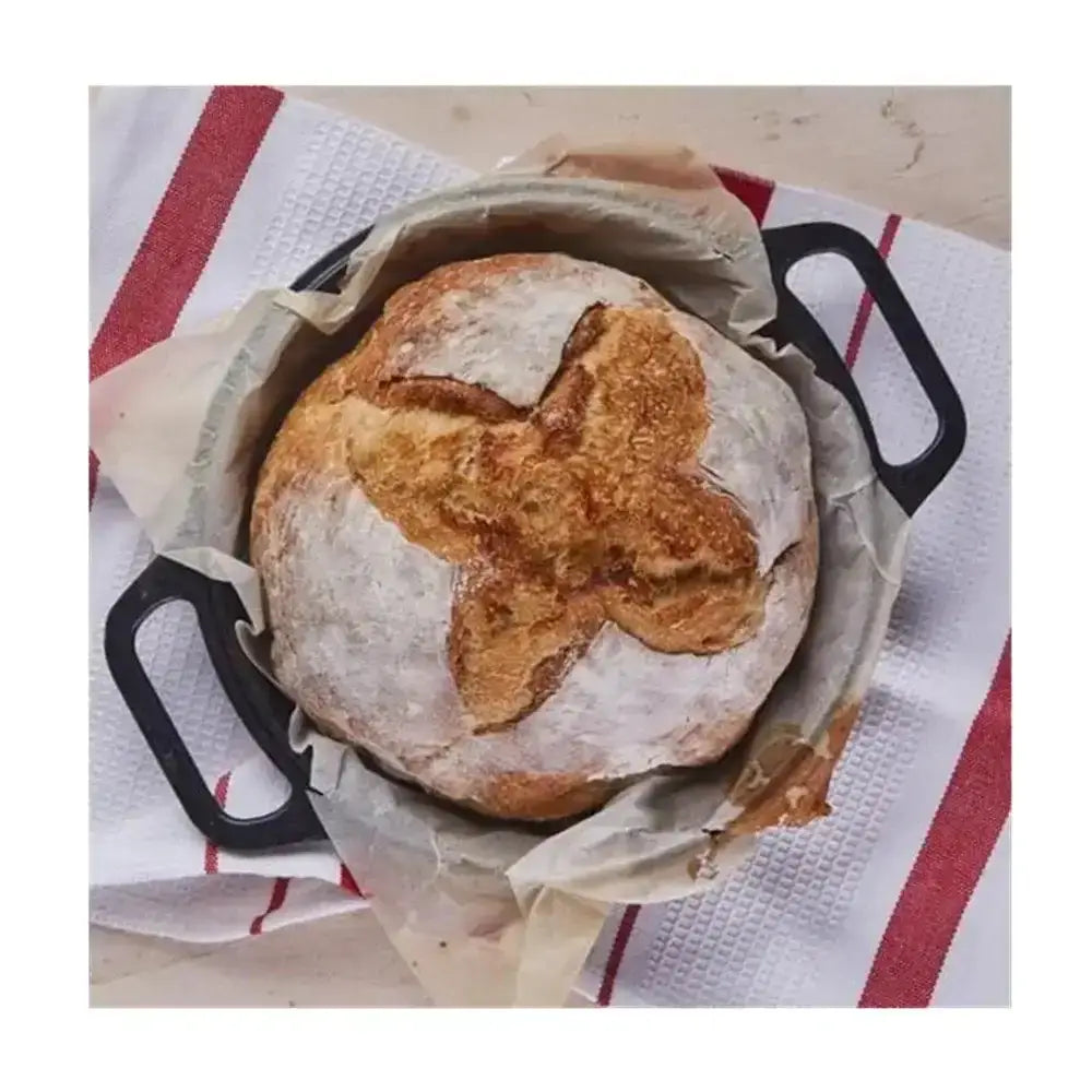Loaf of bread in a black cast iron skillet on a red and white striped towel