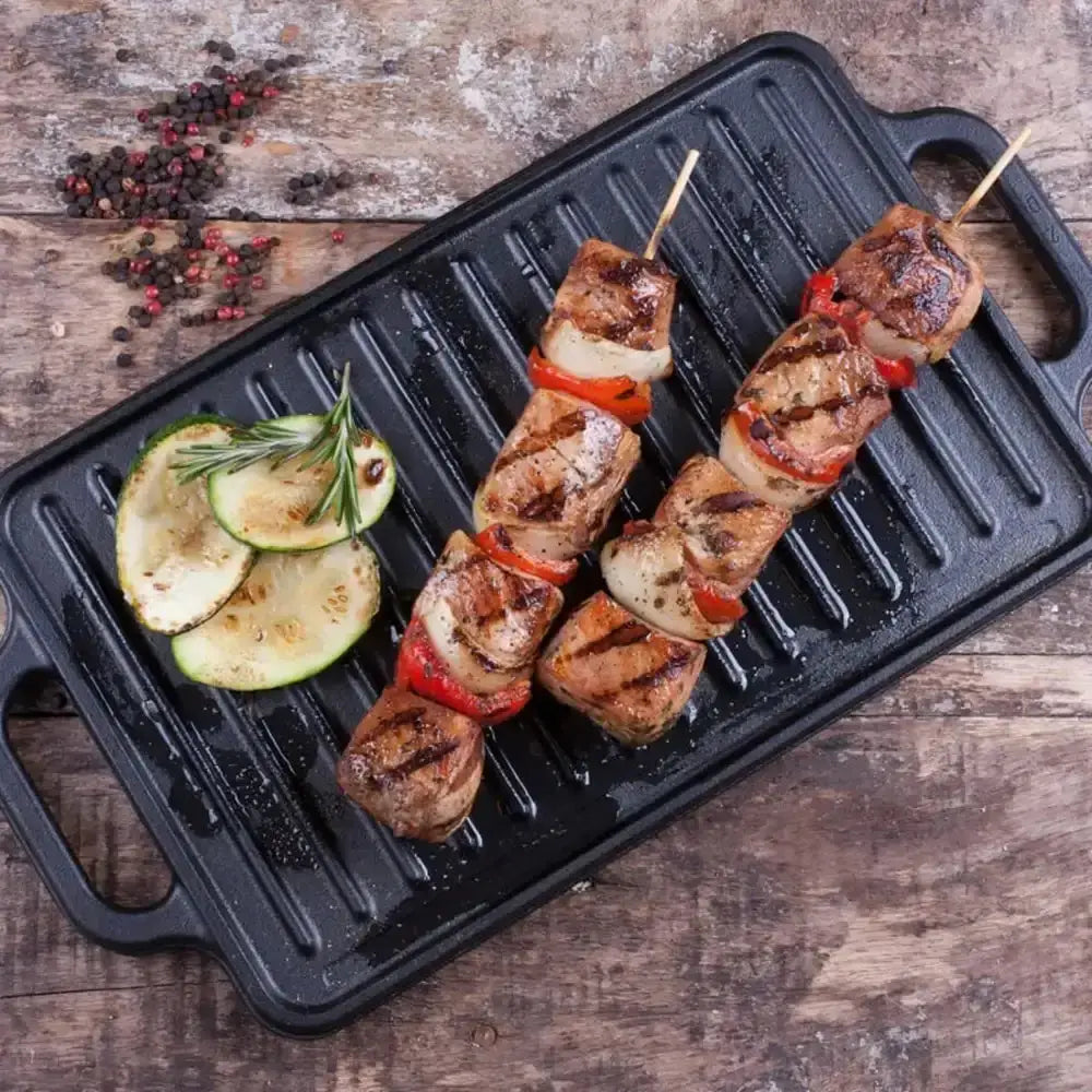 Grilled skewers on a black grill pan with zucchini slices on a wooden surface.