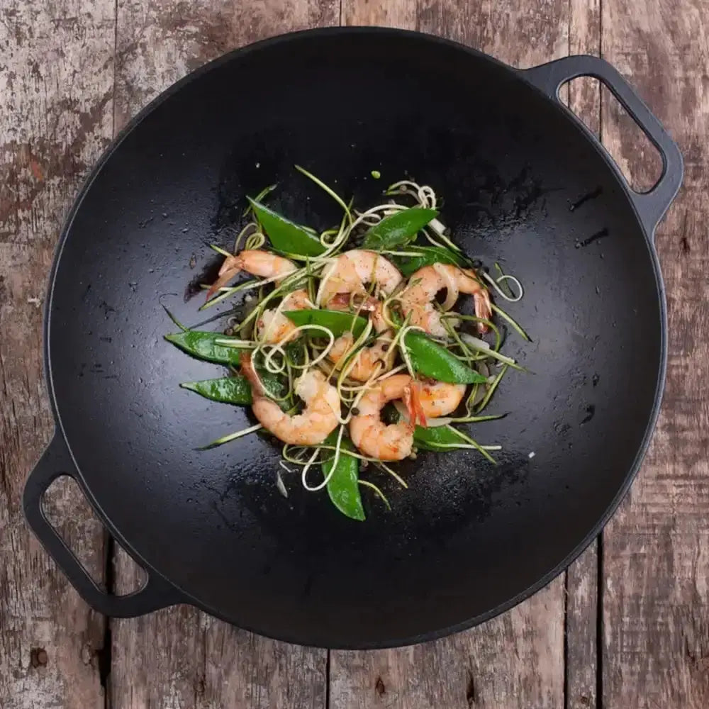 Black wok with shrimp and greens on a wooden surface