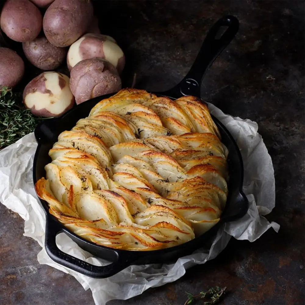 Baked dish in a black skillet with braided top, surrounded by potatoes on a dark surface.