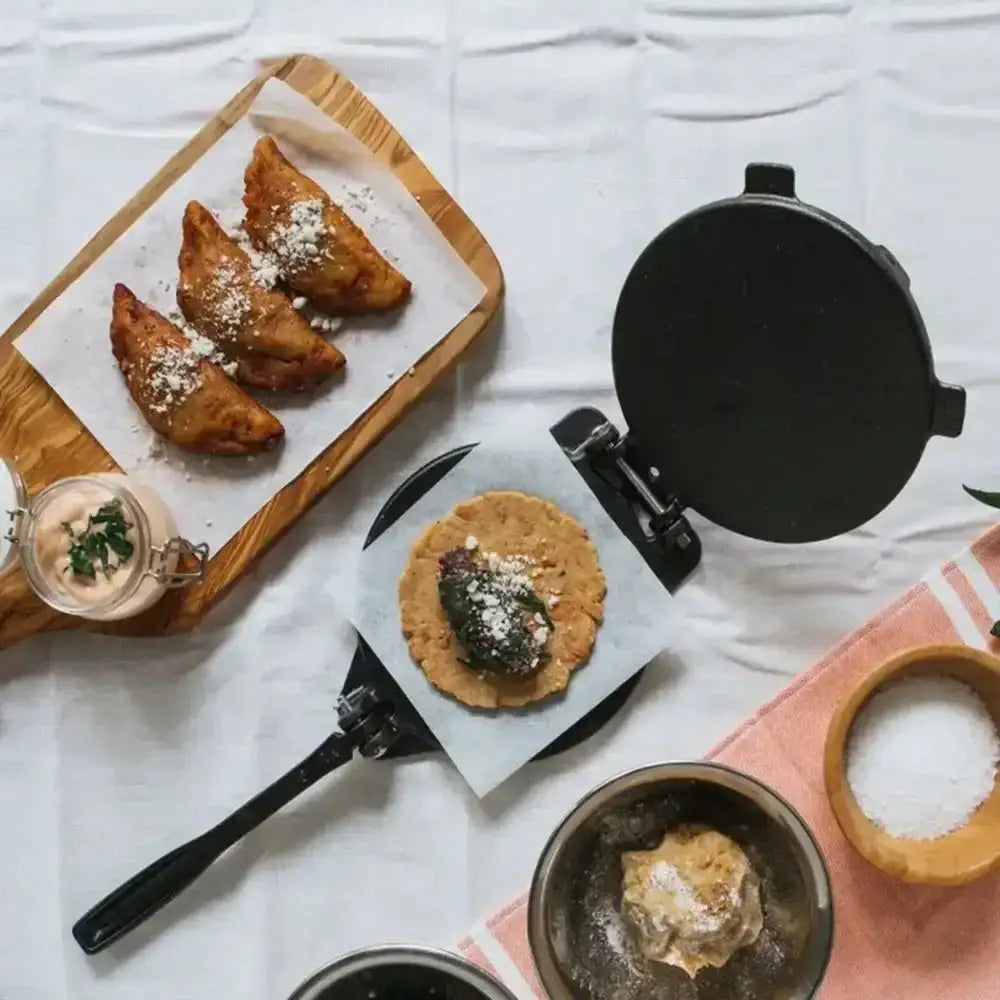 Fried food items on a wooden board with a waffle maker and ingredients on a white surface.