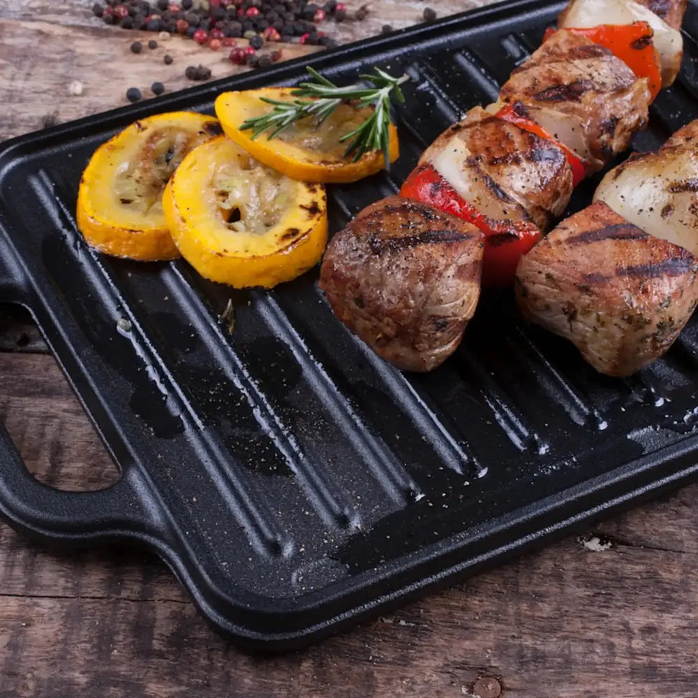 Grilled skewer with meat and vegetables on a black grill pan on a wooden surface.