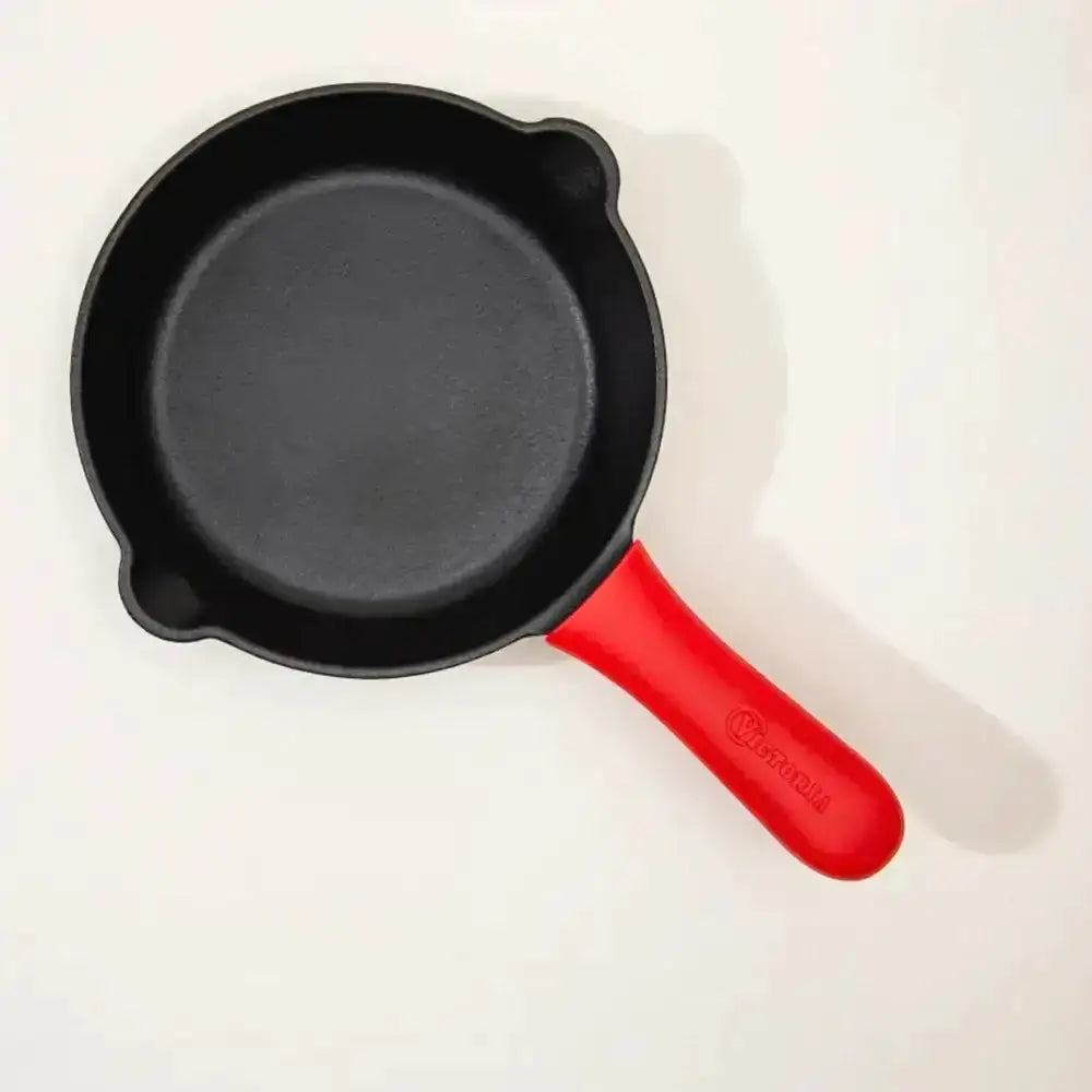 Black frying pan with a large red Victoria silicone handle on a white background
