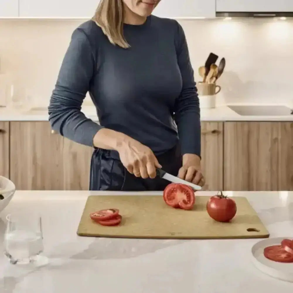 Person cutting tomatoes on a wooden cutting board in a kitchen.