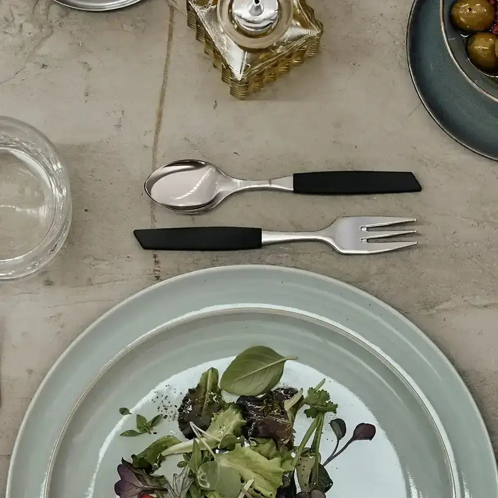 Table setting with a plate of salad, fork, and spoon on a neutral surface.