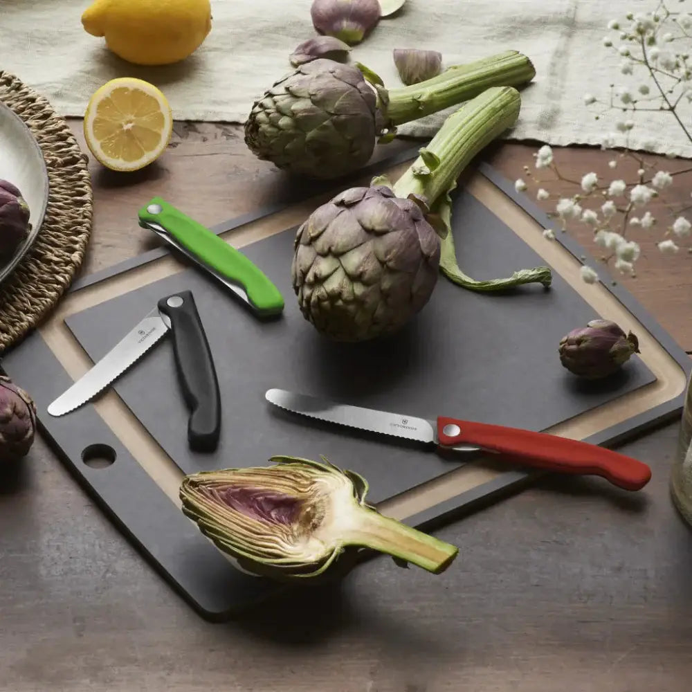 Artichokes on a cutting board with knives and lemons on a wooden surface