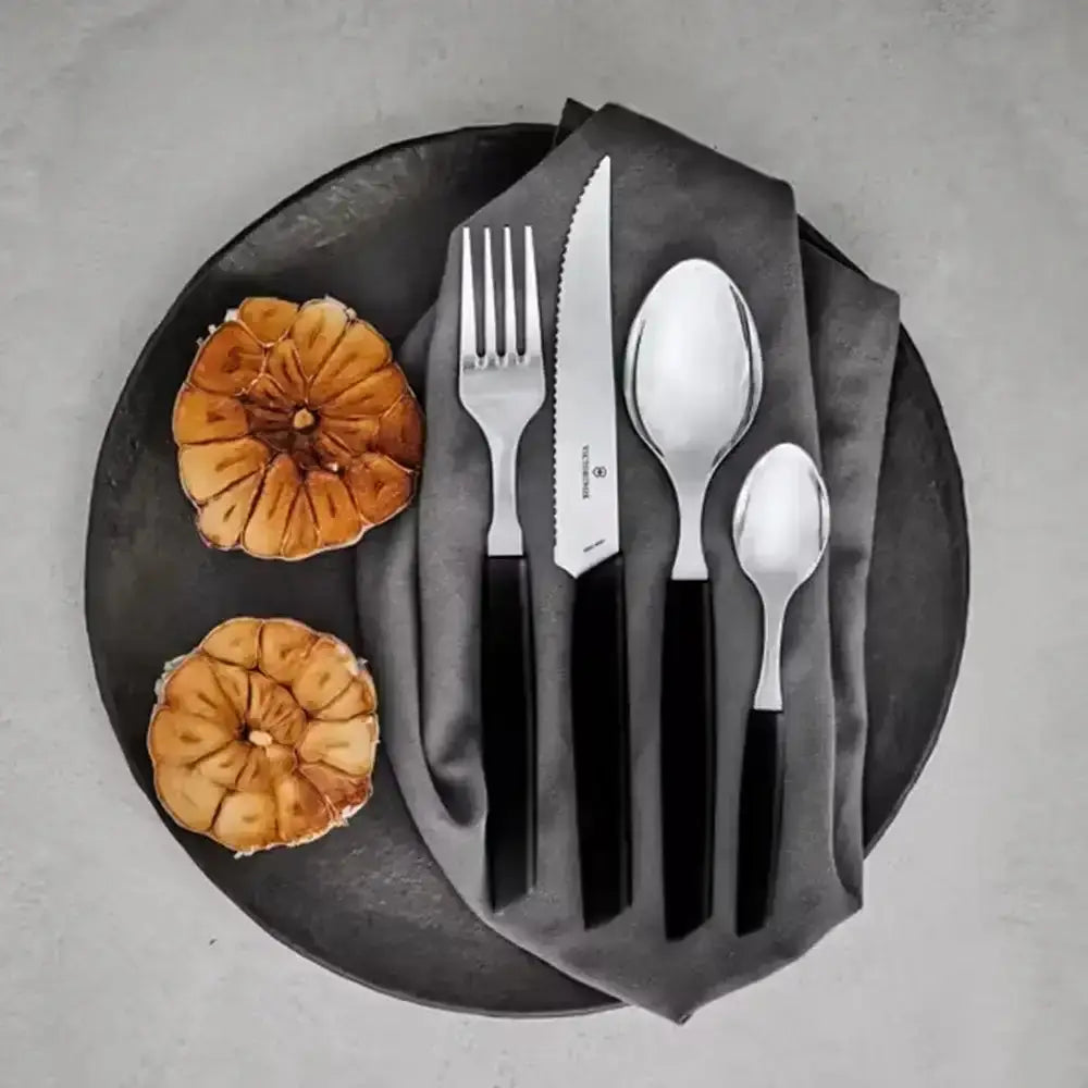 Black plate with silver cutlery and two figs on a gray background