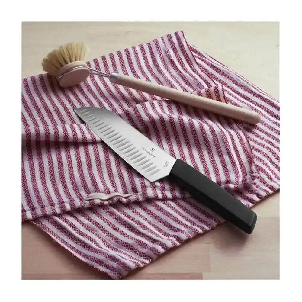 Knife with black handle and wooden blade, brush, and red and white striped towel on a wooden surface