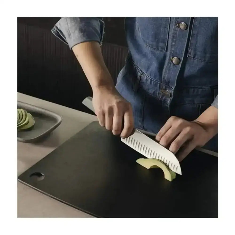 Person cutting avocado on a black cutting board with a knife
