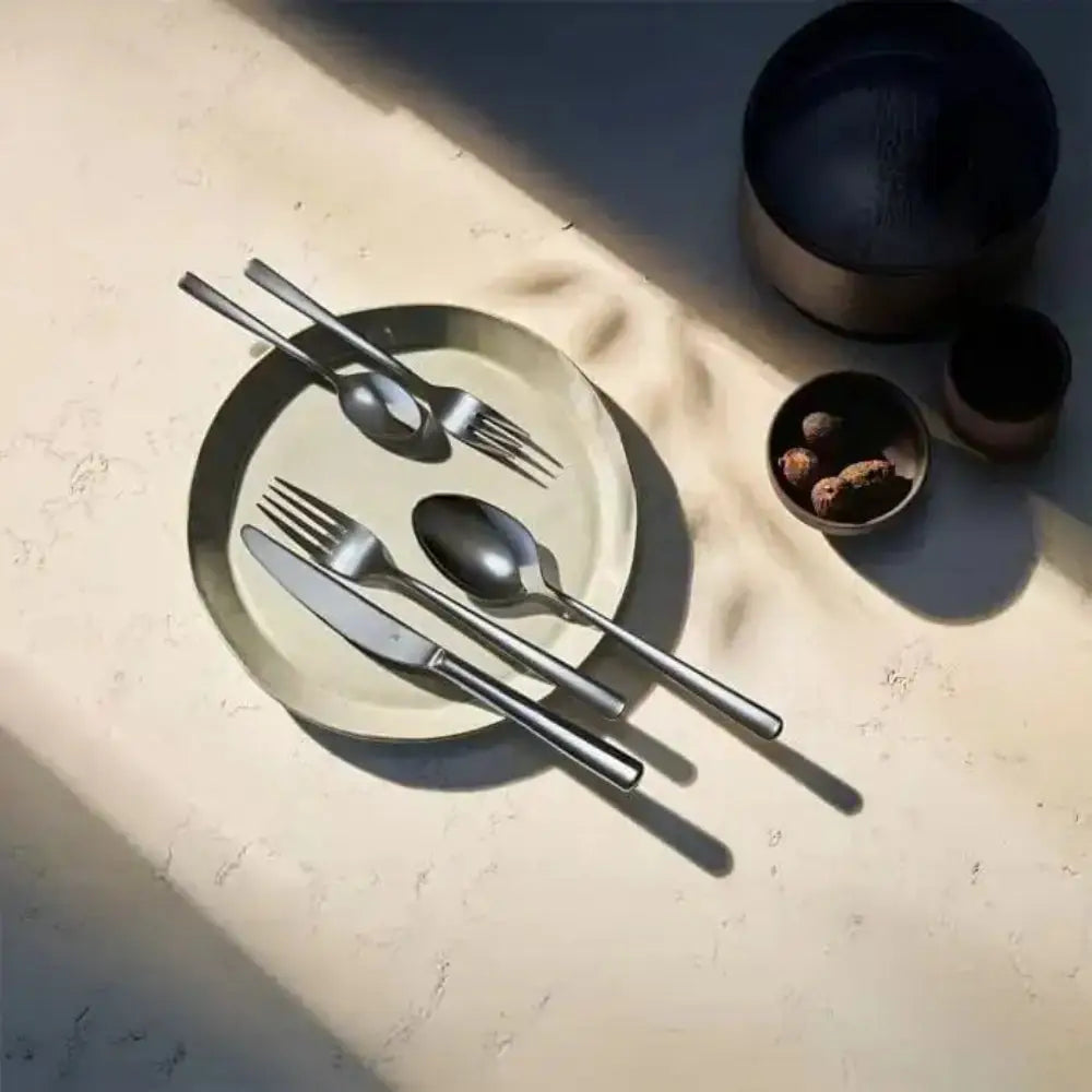 Set of black cutlery on a beige plate with bowls in the background