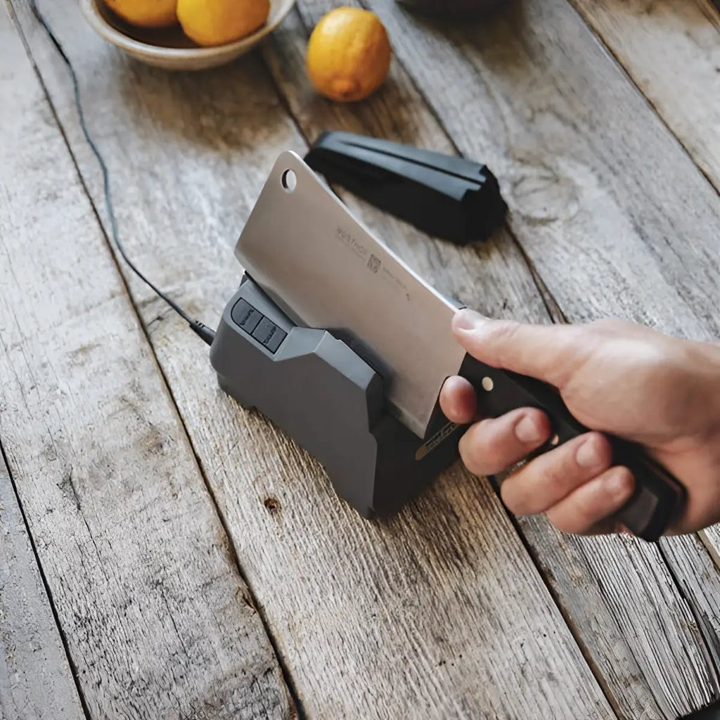 Person using a knife sharpener on a wooden surface with lemons in the background