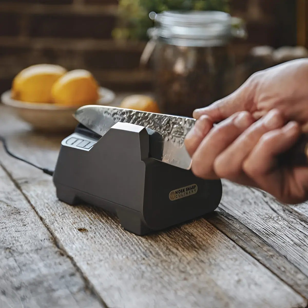 Person sharpening a knife on a black electric sharpener with a rustic wooden surface and blurred background.