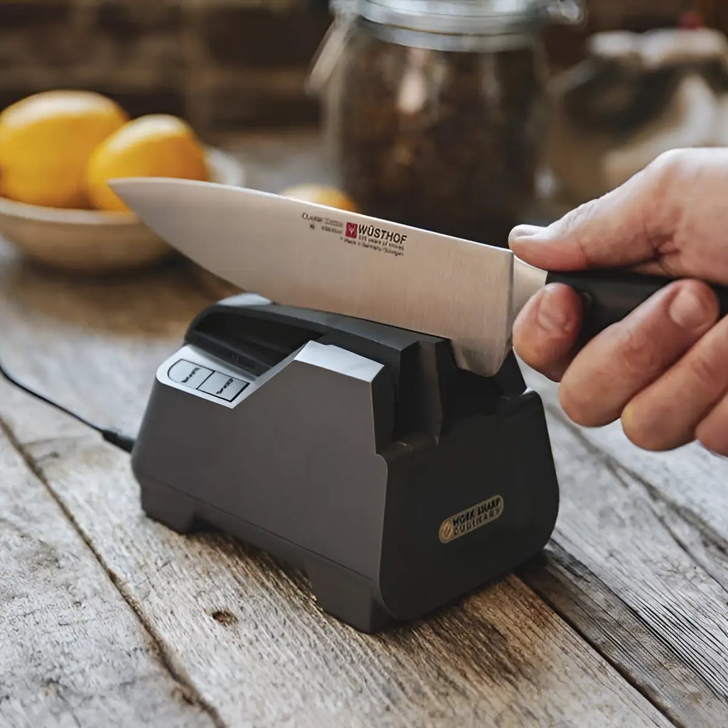 Person sharpening a knife on an electric sharpener with a rustic background
