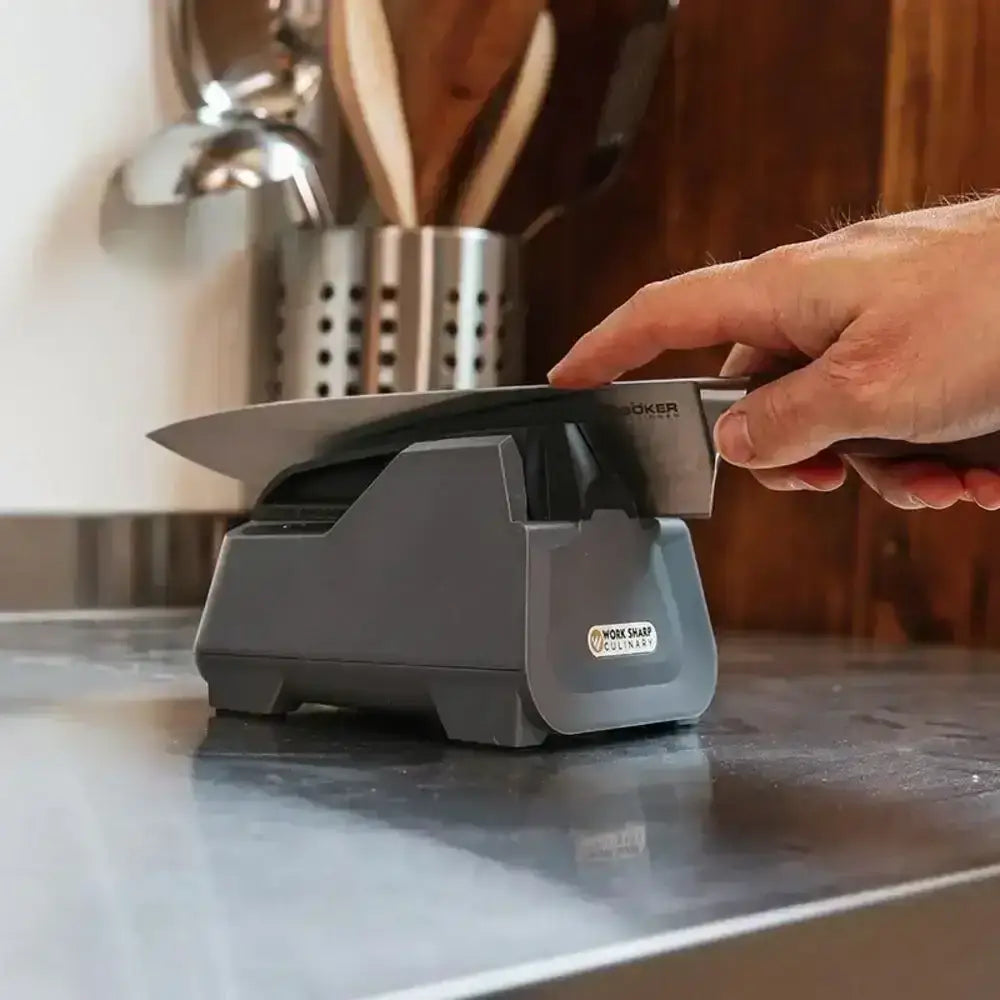 Person using a knife sharpener on a kitchen counter with utensils in the background
