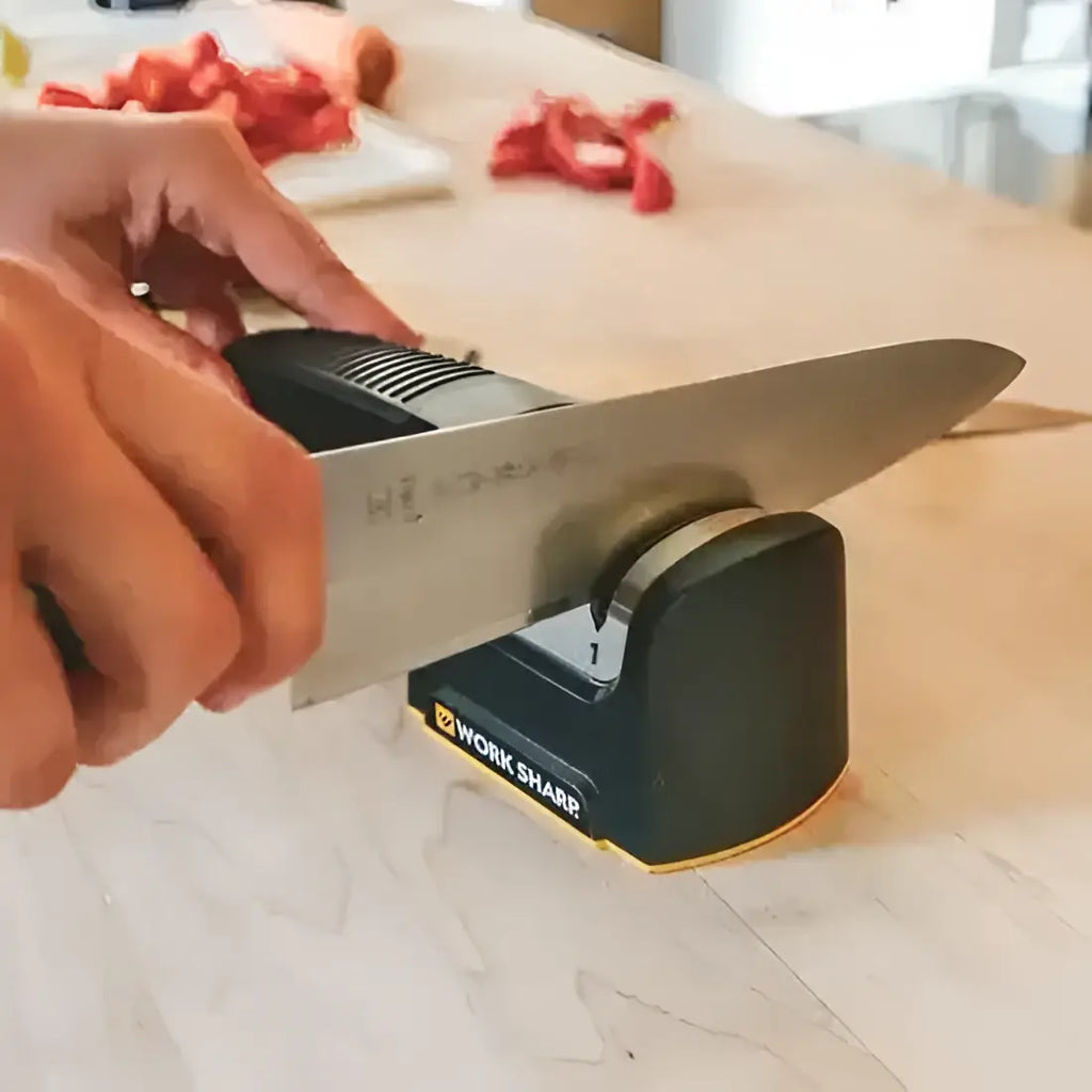 Person sharpening a knife on a 'Work Sharp' sharpener with a blurred kitchen background.