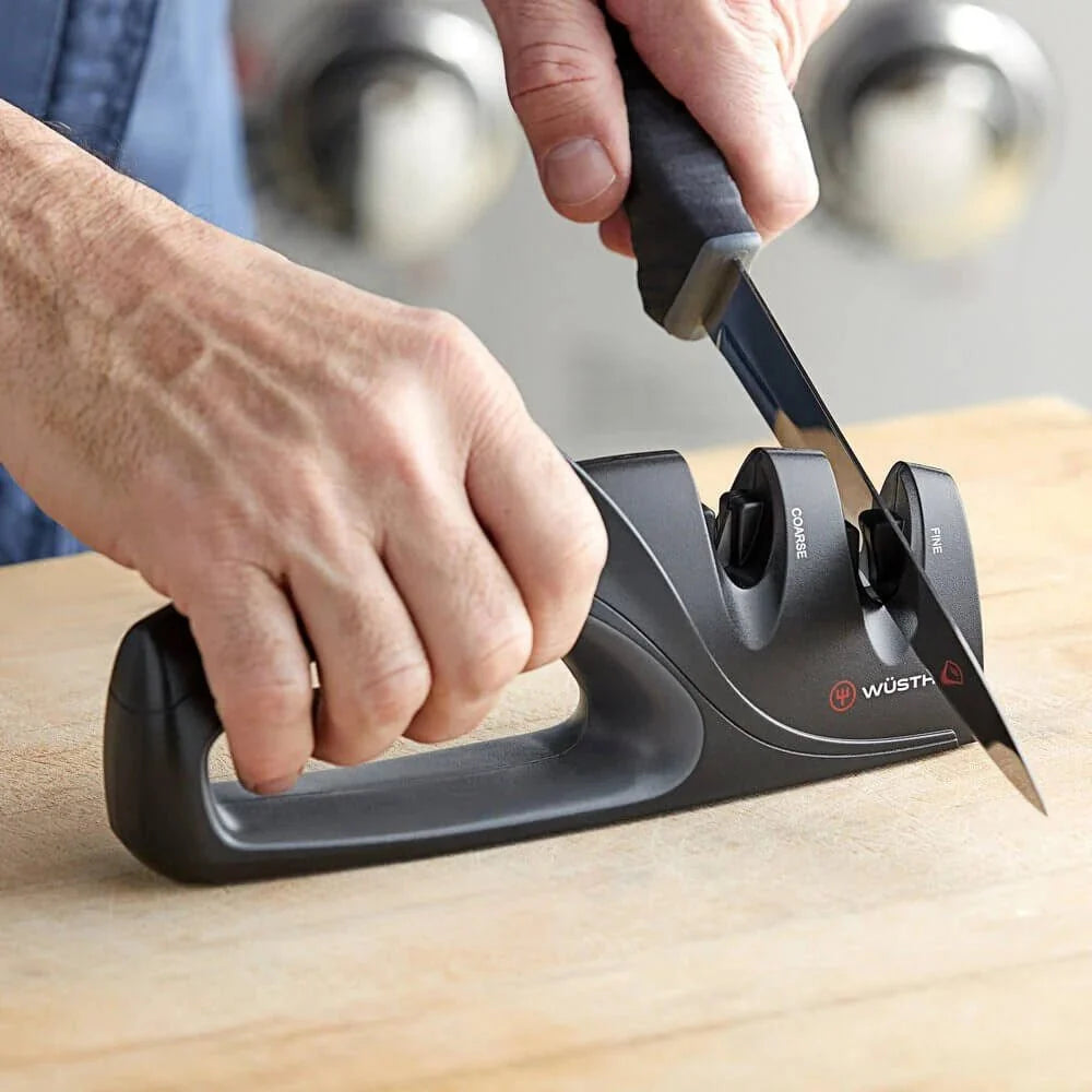 A black Wusthof dual-edge knife sharpener with a ergonomic handle, used to sharpen a knife on a counter