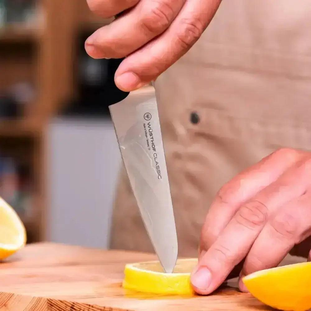 Person cutting a lemon with a Wusthof Classic knife on a wooden cutting board.