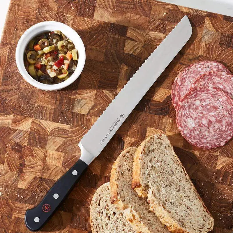 Knife on a wooden cutting board with bread, salami, and olives.