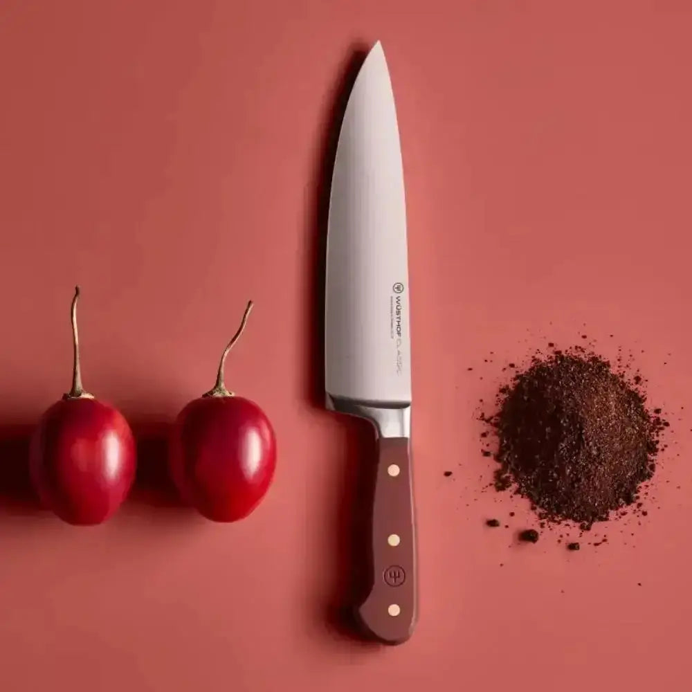 Knife with a brown handle next to two red cherries and a small pile of dark powder on a red background