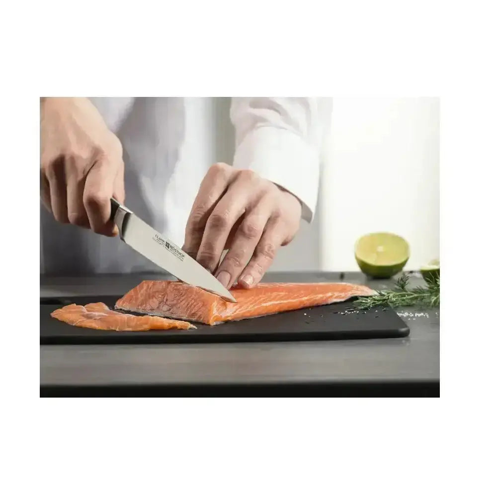 Person cutting salmon with a knife on a cutting board, with a lime and herbs in the background.