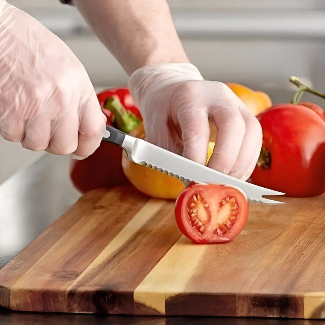 Person cutting a tomato on a wooden cutting board with gloves on