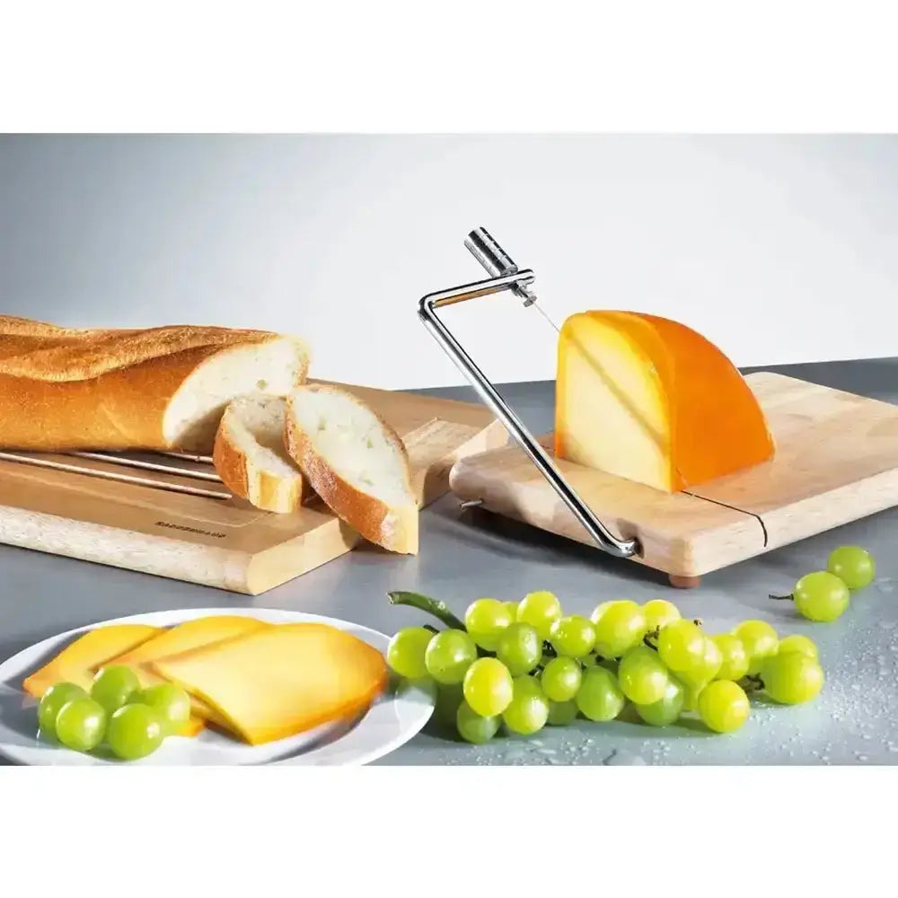 Cheese slicer with a wedge of cheese on a wooden board, surrounded by bread and grapes.