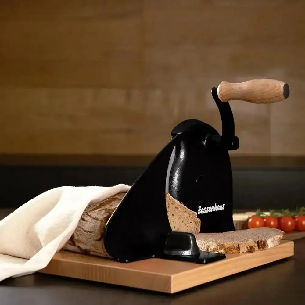 Manual bread slicer on a wooden board with bread and tomatoes against a brown background