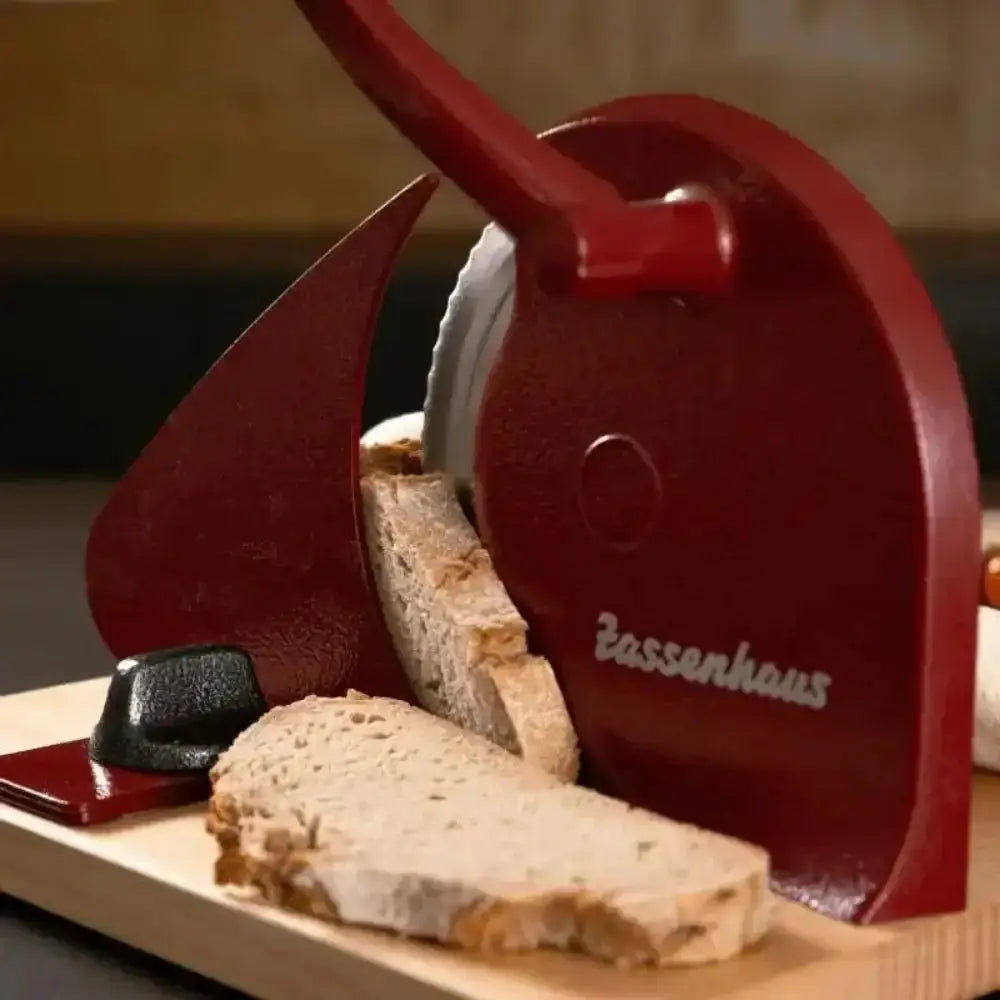 Red manual slicer with 'Zassenhaus' branding on a wooden board with slices of bread.