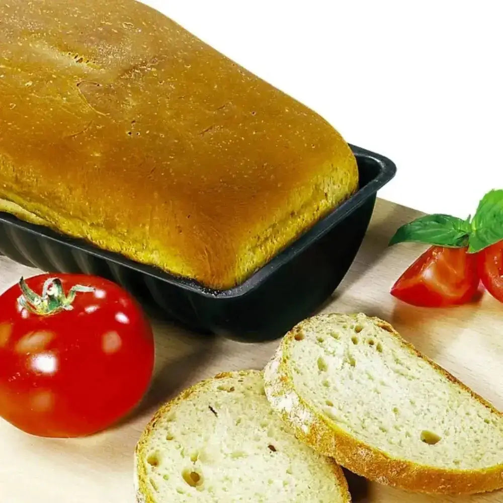 Loaf of bread in a pan with sliced bread and tomatoes on a wooden surface