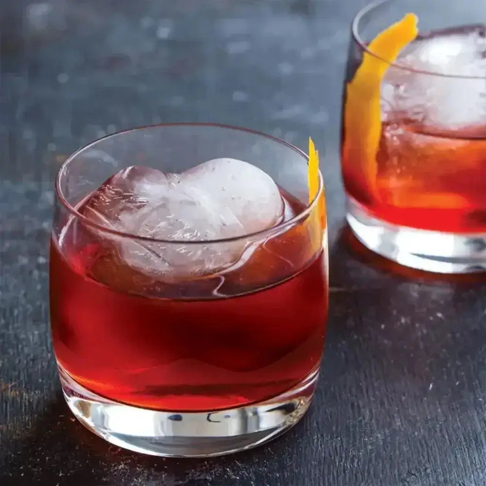 Two red cocktails with ice cubes and orange slices in clear glasses on a dark surface.